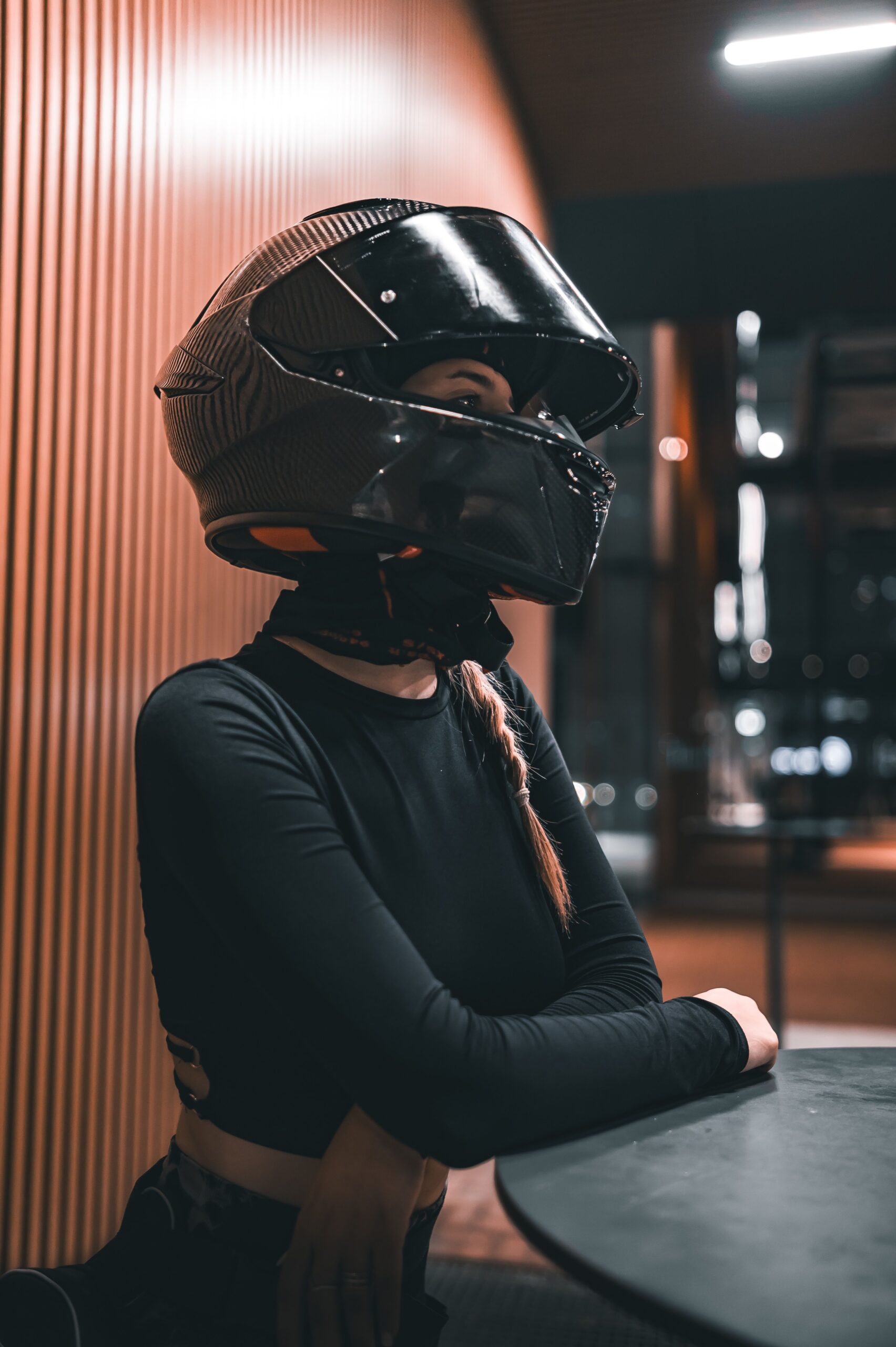 A woman wearing a black motorcycle helmet sits indoors with a reflective visor.